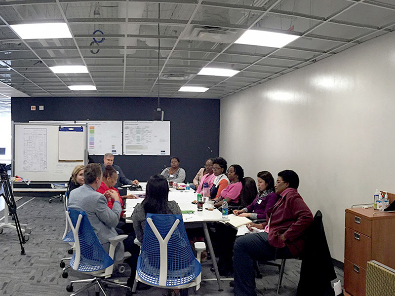 Large group meeting around a conference room table in the SimTigrate Design Lab