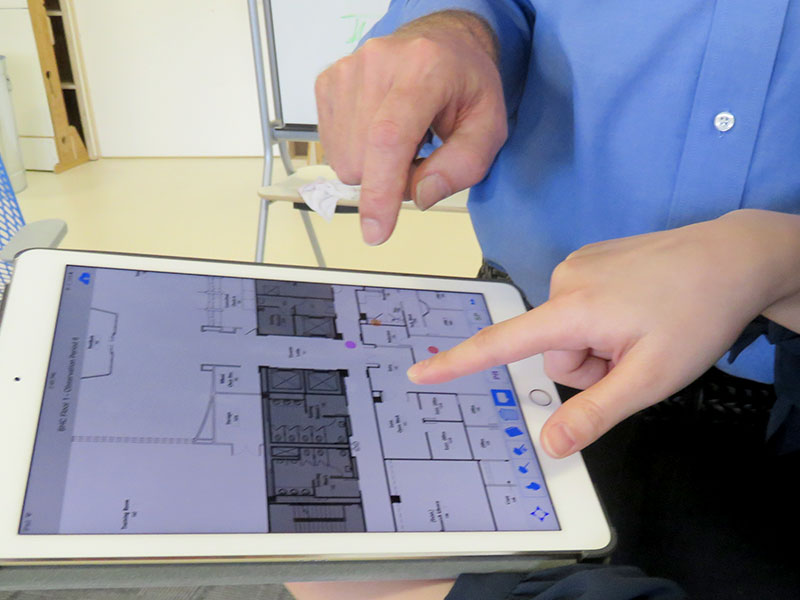 Hands pointing at an iPad as they look at spatial analysis of a floor plan. 