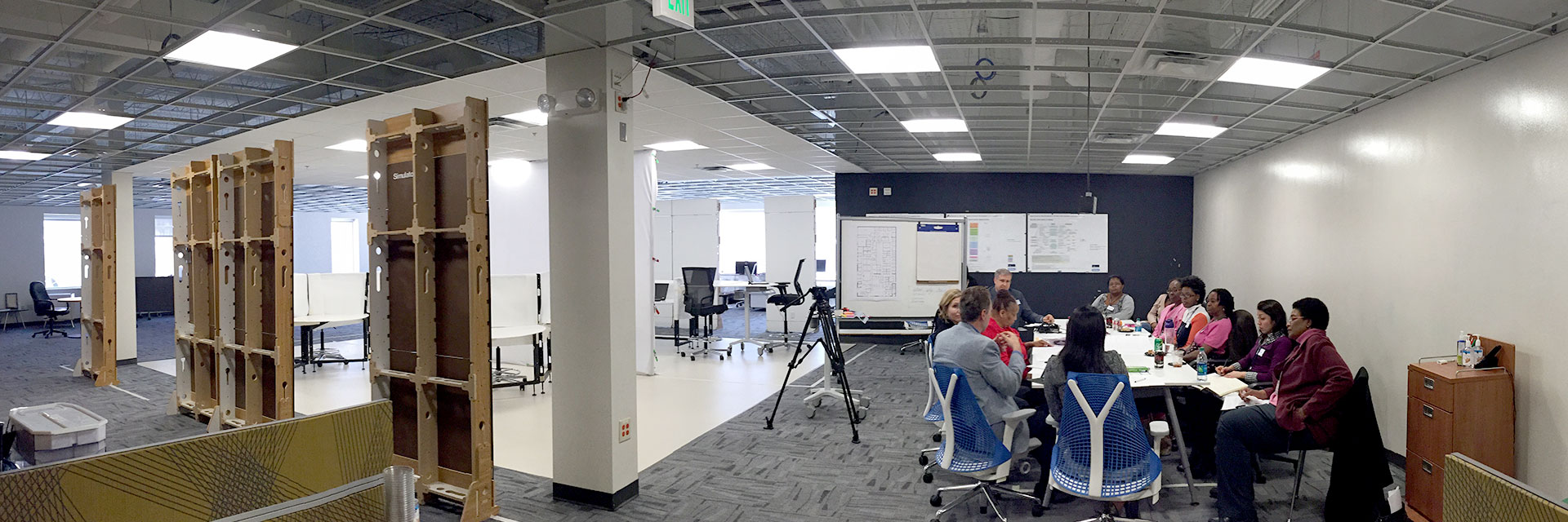 View of the interior of the SimTigrate Design Lab. On the left, there are temporary, flexible labs that can be set up for research scenarios, and on the right, a group of participants are joined together around a conference table. 