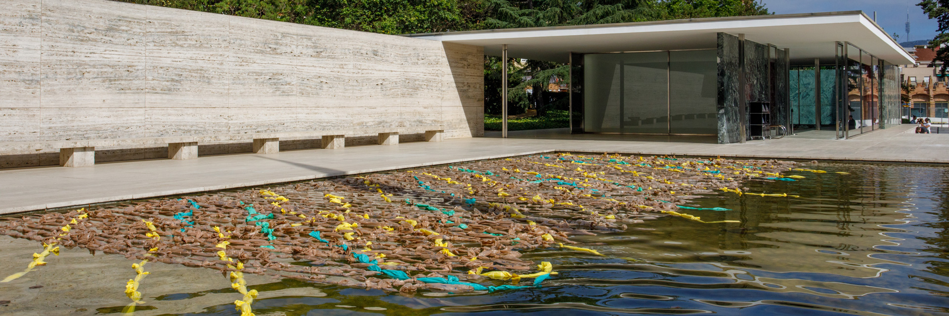 View of reflecting pool at Mies van der Rohe pavilion. A net made of strands of plastic shopping bags covers most of the pool.