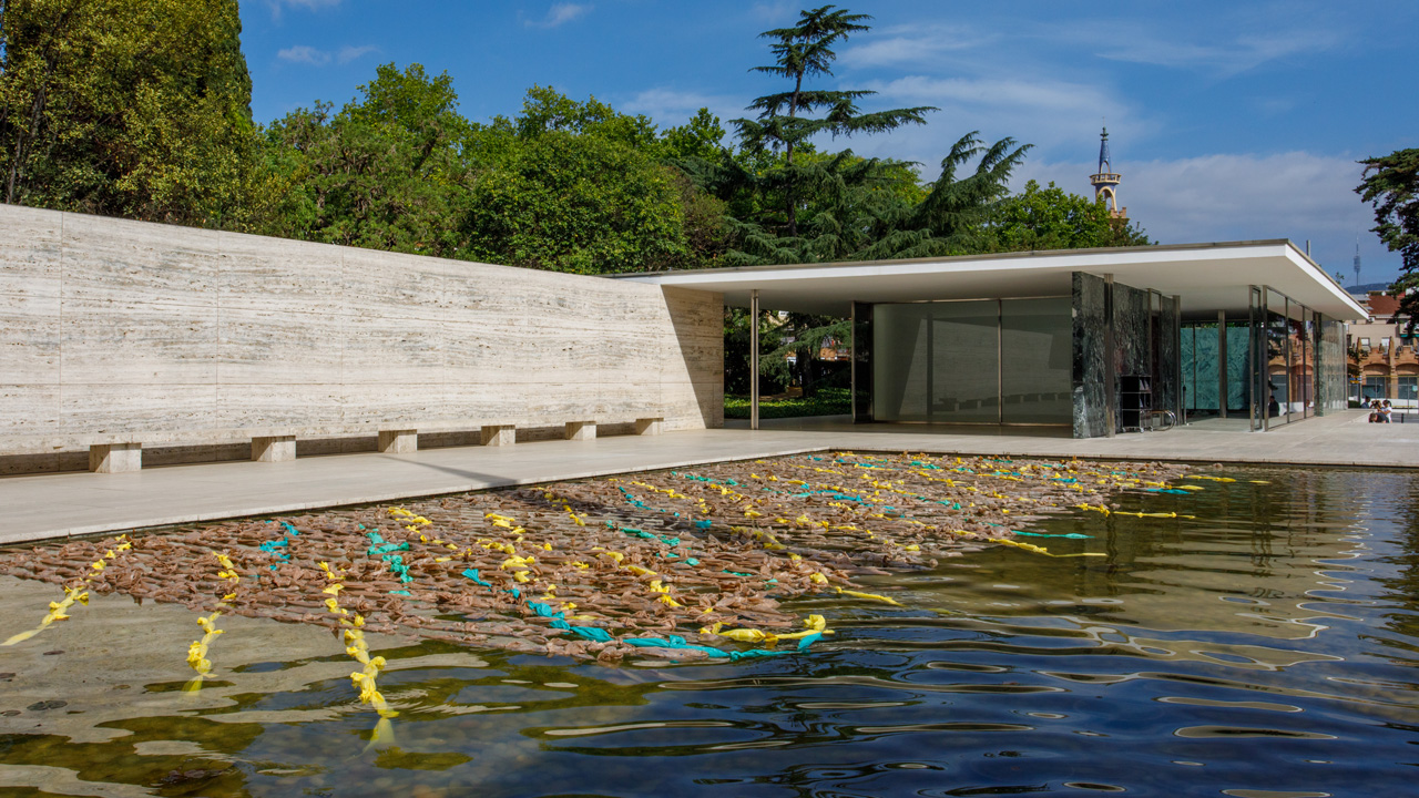 View of reflecting pool at Mies van der Rohe pavilion. A net made of strands of plastic shopping bags covers most of the pool.